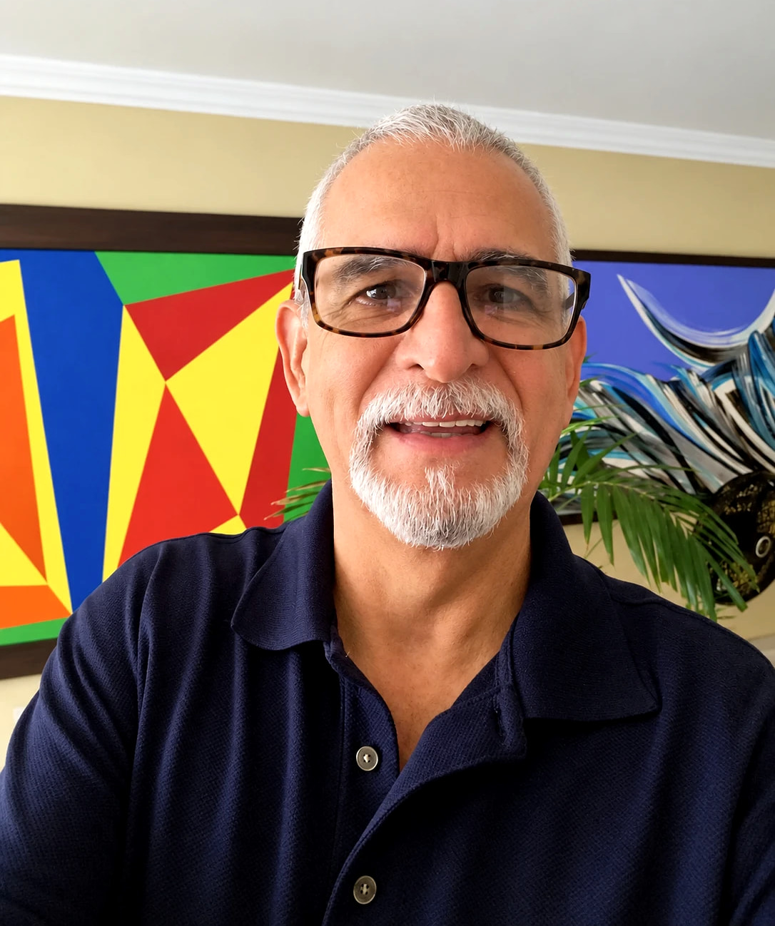 Retrato de David García Esguerra, sonriente, delante de una obra geométrica en rojo, amarillo y azul y otra de olas en azules.