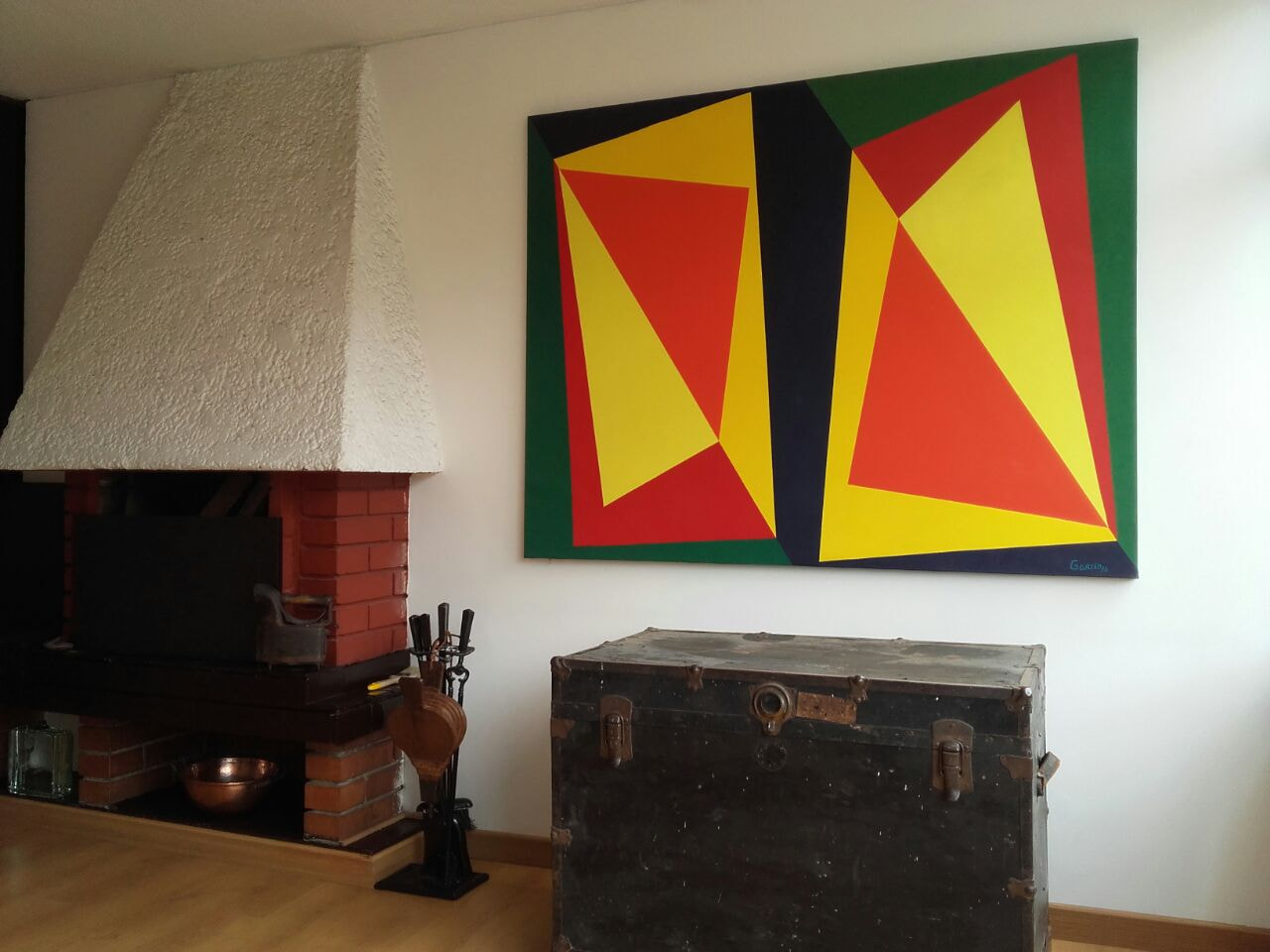 Díptico de triángulos amarillos y rojos sobre verde, colgado junto a una chimenea.
